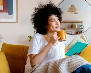 Femme se détendant à la maison avec un livre et une boisson chaude